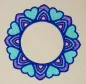 Preview: Stickdatei Set Mandalas + Split Mandala (div. Größen), Foto von Ornament auf hellem Stoff. Buntes Mandala-Ornament in blau-rot-lila aus Herzen und abgerundeten Zacken mit kreisrundem, freiem Zentrum.