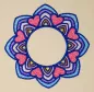 Preview: Stickdatei Set Mandalas + Split Mandala (div. Größen), Foto von Ornament auf hellem Stoff. Buntes Mandala-Ornament in blau-rot-lila-gelb-rosa aus abgerundeten Zacken und Herzen und mit kreisrundem, freiem Zentrum.