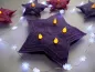 Mobile Preview: Stickdatei Set Christmas Lights (div. Rahmengrößen), Foto zeigt als LED-Cover in Sternformat 1 großen lila Stern mit 4 Öffnungen für Licht, in die leuchtende LEDs eingesteckt sind. Umgeben im Hintergrund von kleineren Sternen ähnlicher Machart.