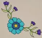 Mobile Preview: Stickdatei Set Folksy Flowers (div. Größen), Foto mit Stickerei auf hellem Stoff. Ornament: türkis-blau-lila Blüte, flankiert von 2 Blütenzweigen in lila-grün.