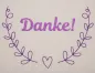 Preview: Stickdatei Set florale Rahmen + Schriftzüge. Foto mit hellem Stoff und pink-lila Bestickung. Durch 2 randgebende Blattranken mit Herz dazwischen wird ein nach oben offenen Rahmen bildet. Innen der Schriftzug "Danke!".