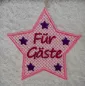Preview: Freebie Stickdatei Für Gäste Handtuchmotiv (10x10), Foto des Emblems auf hellem Frottee. Fünfzackiger Stern in rosa mit dicker Umrandung und filigranem Muster. Darin Schriftzug "Für Gäste" in rot, in jeder Sternzacke kleiner fünfzackiger Stern in lila Vol