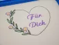 Preview: Stickdatei Set florale Rahmen + Schriftzüge, Foto mit in Stickrahmen eingespanntem hellen Stoff. Darauf Herzumriss mit Schriftzug "Für Dich" im Inneren. Herz wird auf einer Seite durch einen Blüten-Blätter-Zweig verstärkt.