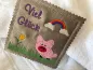 Preview: Stickdatei Set ITH Mini-Grußkarten inkl. Abwandlung zur Geschenktasche, Foto mit 1 quadratischen Ausarbeitung, präsentiert auf hellem Untergrund. Braunes Kunstleder mit bunter Bestickung Schweinchen, Regenbogen, Wiese mit Tulpe, Schriftzug "Viel Glück".