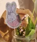 Preview: Stickdatei Set Osterhasen ITH Stabdesigns, Foto mit Designstab, der in einem Glas mit Frühlingsblumen steckt. Osterhase auf grauem Filz, anteilig zu sehen, sitzt in einer halben Ostereierschale. Schmückung an einem Ohr.