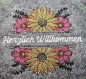 Preview: Stickdatei Set Floral Borders (div. Größen), Foto mit Ausfertigung auf grauem Filz. Arrangement mit Sonnenblume in gelb-orange-pink, ober- und unterhalb des Schriftzugplatzes identisch. Schriftzug in weiß "Herzlich Willkommen".