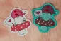 Preview: Stickdatei Set Lovegnomes ITH Stabdesigns, Foto mit 2 Designstäben, beide Motive Gnom in rot/weiß/rosa auf Fliegenpilz, Liebesbrief in der Hand. 1 mal auf weißem Untergrund, 1 mal auf grünem Untergrund.