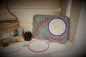 Preview: Freebie Stickdatei ITH Mug Rug Winterzeit (13x18 und 10x10 Rahmen), Foto mit komplettem querformatigem Tassenteppich nebst einzelnem rundem Abstellplatz, umgeben von beigefügten Deko-Elementen. Teppich grau, Abstellplatz beige mit lila Rand und hellem Eis
