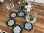 Preview: Stickdatei Set ITH Mug Rug 6, Tischarrangement mit kleinem buntem Blumenstrauß und  sechs kreisförmig ausgelegten Mug Rugs, wobei zwei von ihnen je ein Weinglas tragen. Alle sechs haben einen strahlenförmig und doppelt am Rand abgesteppten dunkelgrauen Fi