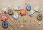 Preview: Stickdatei Set Oster-Stabdesigns, Foto mit 11 Designs, auf Holzuntergrund liegend, dazwischen kleine Dekoelemente als Beigaben. 4 mal Ei mit Herz darin; 2 mal Hasenkopf; 1 mal Küken in Eierschale; 2 mal Blüten;  2 mal Doppel-Osterei.