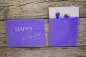 Preview: Stickdatei Set ITH Geburtstagskarten (10x10 u. 13x18), Foto mit 2 lila Karten. Karte im Hochkantformat zeigt ihre Rückseite, die eine Einstecktasche aufweist, aus der 2 Bonbonpapierspitzen ragen.Karte im Querformat zeigt Bestickung: "HAPPY Birthday!"/Str