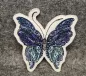 Preview: Stickdatei Schmetterling Vollstickmotiv, Foto mit Ausfertigung auf dunkelgrauem Untergrund. Motiv: Schmetterling in lila-blau-türkis-schwarz.