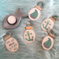 Preview: Stickdatei Set christliche Deko und Gastgeschenke (ITH), Foto zeigt 5 ovale Anhänger mit geklammertem Metallbügel als Öse, darin Schlüsselring. 2 mal Segelboot, 2 mal Anker, 1 mal Fischsymbole mit Aufschrift "Max 5.9.20".