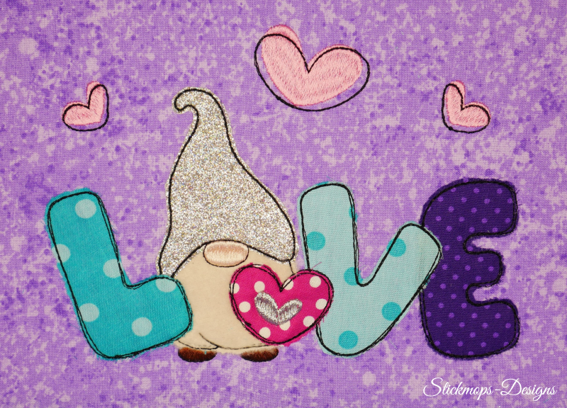 Preview: Stickdatei Set 5in1 Lovegnome Doodle-Applikationen, Foto mit Applikation auf lila-hell gemustertem Stoff. Bunter Schriftzug 