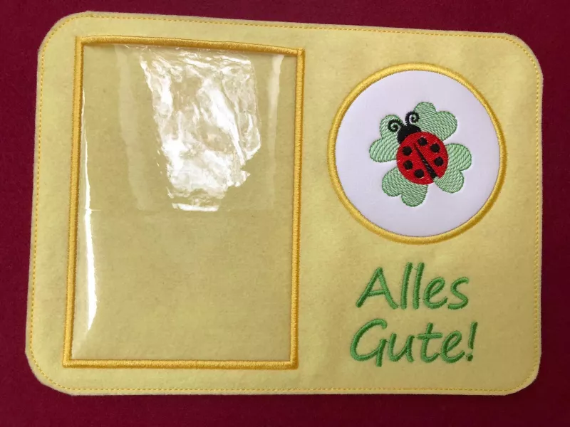 Mugrug aus gelbem Filz mit Einsteckfach. Auf dem Tassenplatz ist ein Marienkäfer mit Kleeblatt abgebildet und darunter der Schriftzug "Alles Gute".