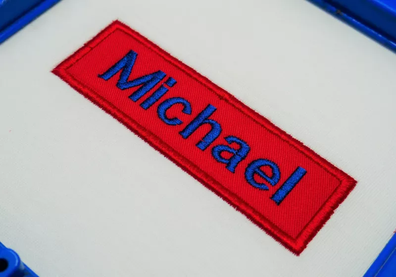 Stickdatei Set Blanko-Patches Aufnäher (mit und ohne Klett auf der Rückseite umsetzbar), Foto zeigt roten länglichen Aufnäher mit blauem Schriftzug "Michael" auf hellem Stoff.