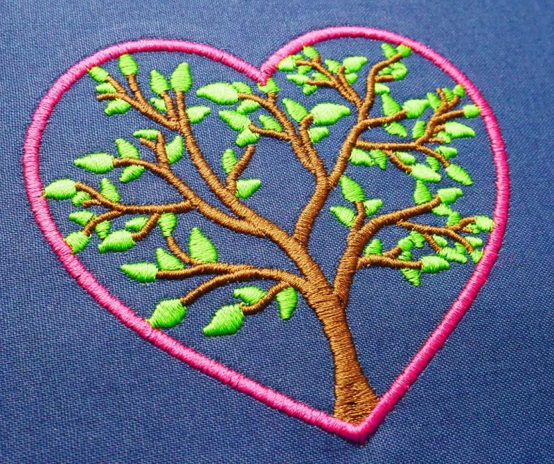 Stickdatei Set Monogramm Motiv Baum inkl. ITH Schild. Foto zeigt auf dunkelblauem Stoff pinken Herzumriss, darin ein grün-brauner Baum, der den ganzen Raum ausfüllt.