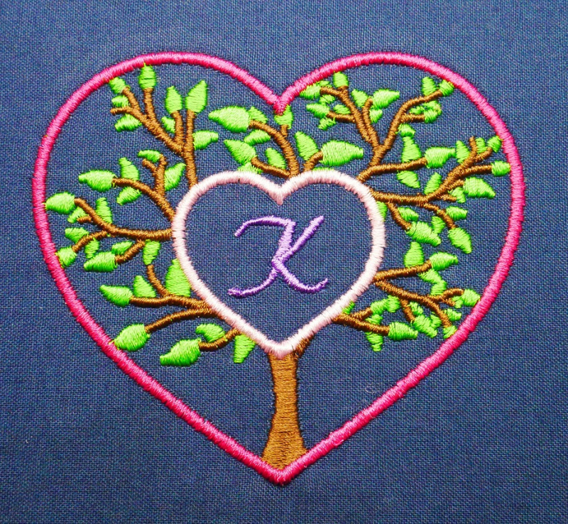Preview: Stickdatei Set Monogramm Motiv Baum inkl. ITH Schild, Foto zeigt pinken Herzumriss auf dunkelblauem Stoff. Innerhalb des Herzumrisses Baum mit grünen Blättern, Zentrum ausgespart und gefüllt mit kleinem rosa Herzumriss, das den Buchstaben 