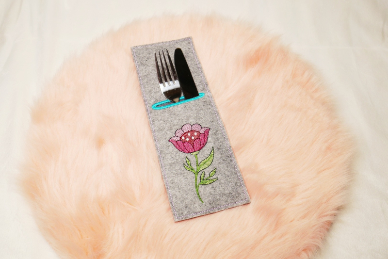 Preview: Stickdatei Set ITH Bestecktaschen Folksy Flowers (4 Größen), Foto zeigt rechteckige Hochkant-Tasche, mittelgrauer Filz, befüllt mit Besteck. Bestickung mit buntem Blumenmotiv mit Stengel/Blättern.