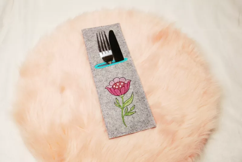 Stickdatei Set ITH Bestecktaschen Folksy Flowers (4 Größen), Foto zeigt rechteckige Hochkant-Tasche, mittelgrauer Filz, befüllt mit Besteck. Bestickung mit buntem Blumenmotiv mit Stengel/Blättern.