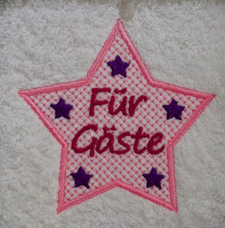 Freebie Stickdatei Für Gäste Handtuchmotiv (10x10), Foto des Emblems auf hellem Frottee. Fünfzackiger Stern in rosa mit dicker Umrandung und filigranem Muster. Darin Schriftzug "Für Gäste" in rot, in jeder Sternzacke kleiner fünfzackiger Stern in lila Vol