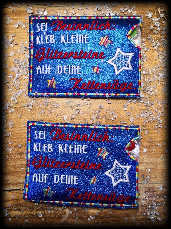 Stickdatei Set ITH Hüllen für Adventskalender to go, Foto mit 2 identischen querformatigen Ausfertigungen auf glitzerndem Holzuntergrund. Hüllen in glitzernd-blau mit Sternenstick und Aufschrift: "SEI Besinnlich: KLEB KLEINE Glitzersteine AUF DEINE Ketten