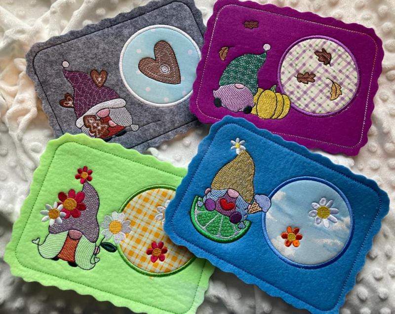 Preview: Stickdatei Set Gnom Mug Rugs 4 Jahreszeiten + Einzelmotive, Foto mit 4 bunten Tassenteppichen aus am Rand gebuchtetem rechteckigem Filz mit je Gnom linksseitig und Tassenabstellplatz (bedruckter Stoff mit diversem Motivstick darauf) rechtsseitig. Frühling