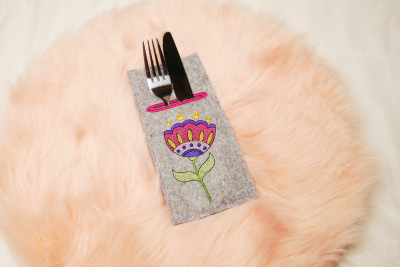 Preview: Stickdatei Set ITH Bestecktaschen Folksy Flowers (4 Größen), Foto zeigt rechteckige Hochkant-Tasche, mittelgrauer Filz, befüllt mit Besteck. Bestickung mit buntem Blumenmotiv.