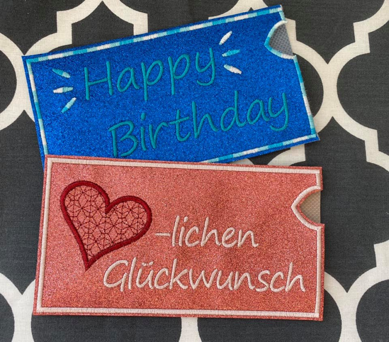 Stickdatei Set ITH Motivhüllen für viele Anlässe für Schokolade, Gutscheine u.a., Foto zeigt 2 rechteckige querformatige Hüllen in orange und mittelblau. Eine mit "Happy Birthday" und Strahlen, eine mit "Herz-lichen Glückwunsch" mit Herz statt Buchstaben.