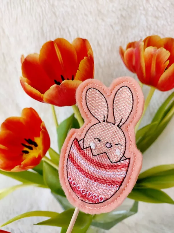 Stickdatei Set Osterhasen ITH Stabdesigns, Foto mit Designstab vor Tulpenstrauß. Auf apricotfarbenem Filz gestickter Osterhase, der in halber Eierschale sitzt.