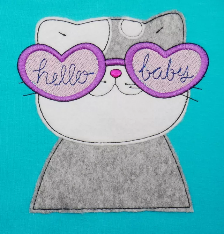 Stickdatei Set Beach Time Cat Doodle Applikation inkl. ITH Anhänger, Foto zeigt auf türkisem Stoff Katzenbüste in grau-weiß als Applikation. Pink-rosa Herz-Brille mit Aufschriften "hello" und "baby".