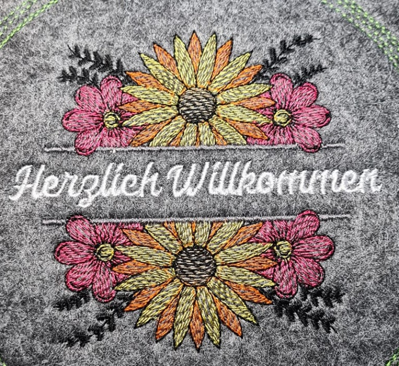 Preview: Stickdatei Set Floral Borders (div. Größen), Foto mit Ausfertigung auf grauem Filz. Arrangement mit Sonnenblume in gelb-orange-pink, ober- und unterhalb des Schriftzugplatzes identisch. Schriftzug in weiß 