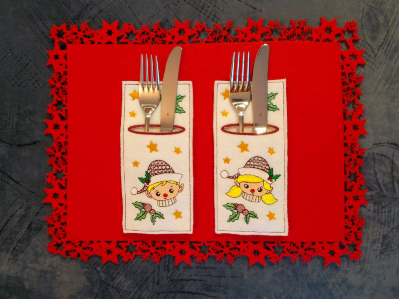 Stickdatei Set ITH Bestecktaschen Christmas Faces, Foto mit 2 länglichen Taschen auf rotem Zierdeckchen, bestückt mit Gabel und Messer. Heller Filz, Bestickung: Jungen-, bzw. Mädchenkopf mit Mütze; Stechpalmenzweige, Sterne.