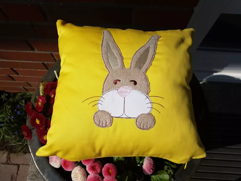 Stickdatei Set XXL Hase Charlie in 3 Variationen, Foto von gelbem Kissen mit Applikation. Sitzender braun-weißer Hase, sichtbar nur dessen Kopf mit Vorderpfoten.