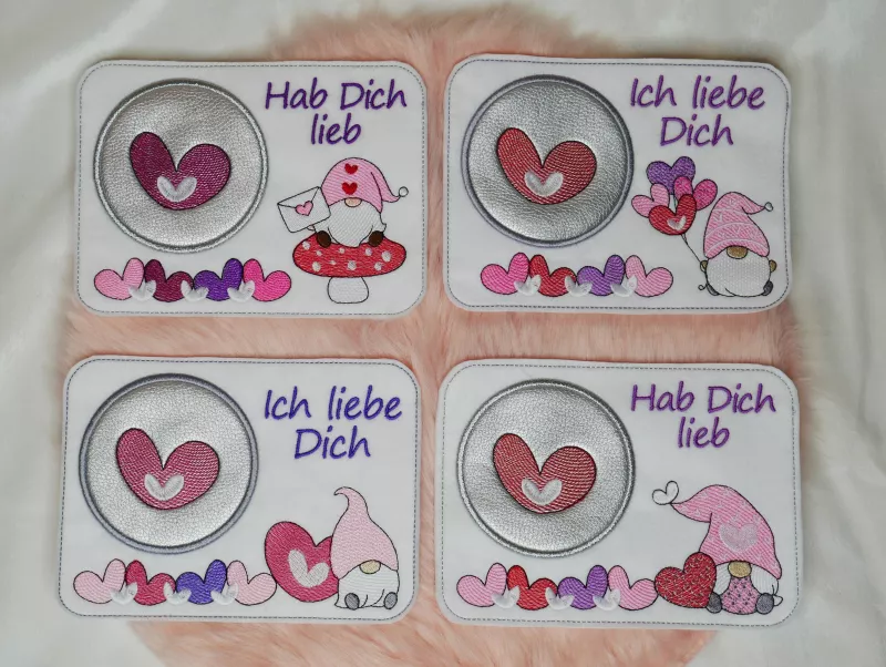 Stickdatei Set Lovegnomes ITH Mugrugs, Foto mit 4 Ausfertigungen, auf apricotfarbenem Fell liegend.
hellem Untergrund mit Becher, Holzherz und Blattzweig als Dekobeigabe. Rechteckige helle Tassenteppiche mit unterschiedlichen bunten Gnommotiven und kreisr