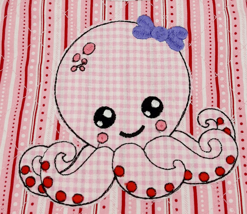 Stickdatei Octopus Applikation für Mädchen, Foto zeigt Oktopus aus rosa-weiß kariertem und besticktem Stoff auf rot-rosa-weiß gestreiftem/gepunktetem Stoff. Dicke lila Stickschleife am Kopf.