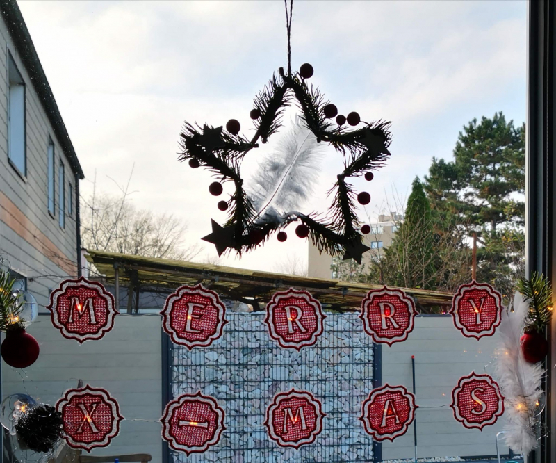 Stickdatei Set Monogramme Barock geeignet für Frottierwaren. Foto zeigt unter einem hängenden Weihnachtsdekostern zwei Reihen mit je 5 aufgereihten Buchstaben in rot-weiß, die "MERRY CHRISTMAS" ergeben.
