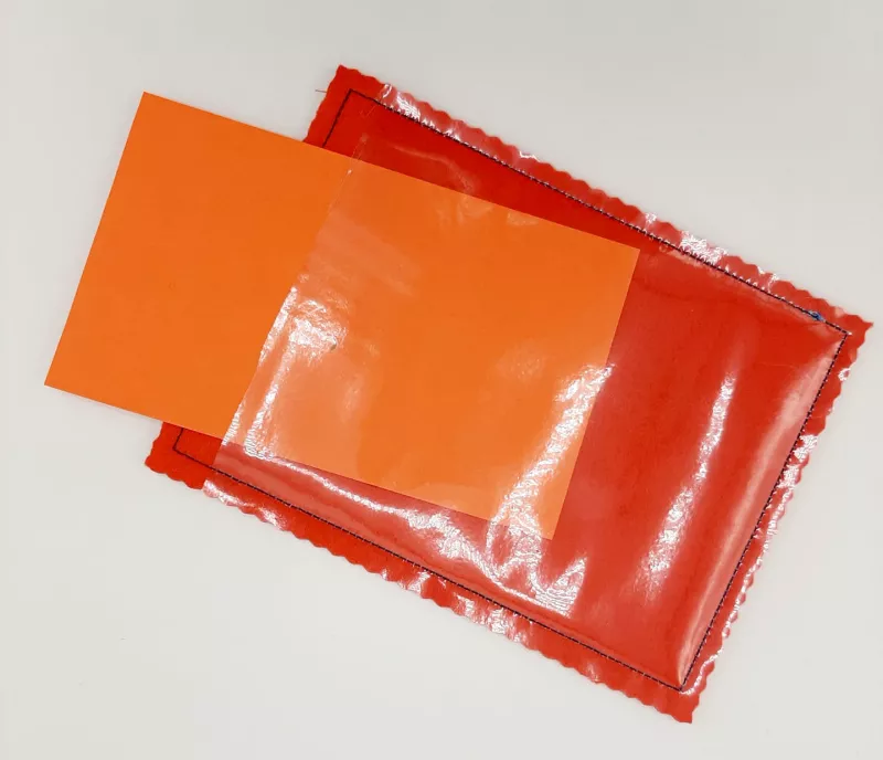 Stickdatei Set ITH Geburtstagskarten (10x10 u. 13x18), Foto mit einer Blankokarte in orangerot mit transparenter Folie, die an einer Seite nicht vernäht ist. Ein auf dem Bild teilweise eingeschobener Papierstreifen macht die transparente Folie, unter die