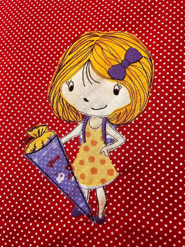 Stickdatei Set Schulkind Sophie (div. Rahmengrößen), Foto eines bunten Motivs auf rot-weiß gepunktetem Stoff. Blondes Mädchen im Kleid (gelb, orange Punkte) mit lila Haarschleife mit lila-gelber und verzierter Schultüte in einer Hand.