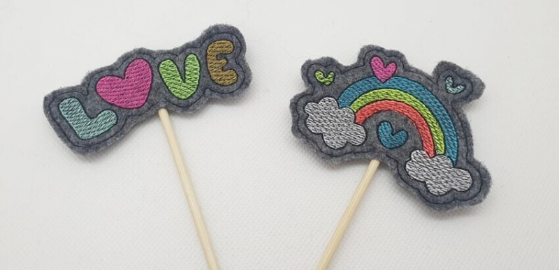 Preview: Stickdatei Set Valentinsmöpse ITH Stabdesigns für Stabdeko Preview: Stickdatei Set Valentinsmöpse ITH Stabdesigns für Stabdeko, Foto mit zwei Designs auf jeweils anthrazitfarbenem Filzuntergrund. Einmal bunter Schriftzug