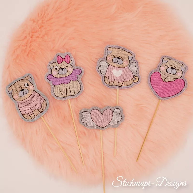 Stickdatei Set Valentinsmöpse ITH Stabdesigns für Stabdeko, Foto fünf unterschiedlicher Designs, präsentiert auf orangem Fellstück. Vier Möpse am Stab: Mops mit Zwinkerauge und Jäckchen, Mops mit Zwinkerauge, Ohrschleife und Halskrause, Mops mit Flügeln,