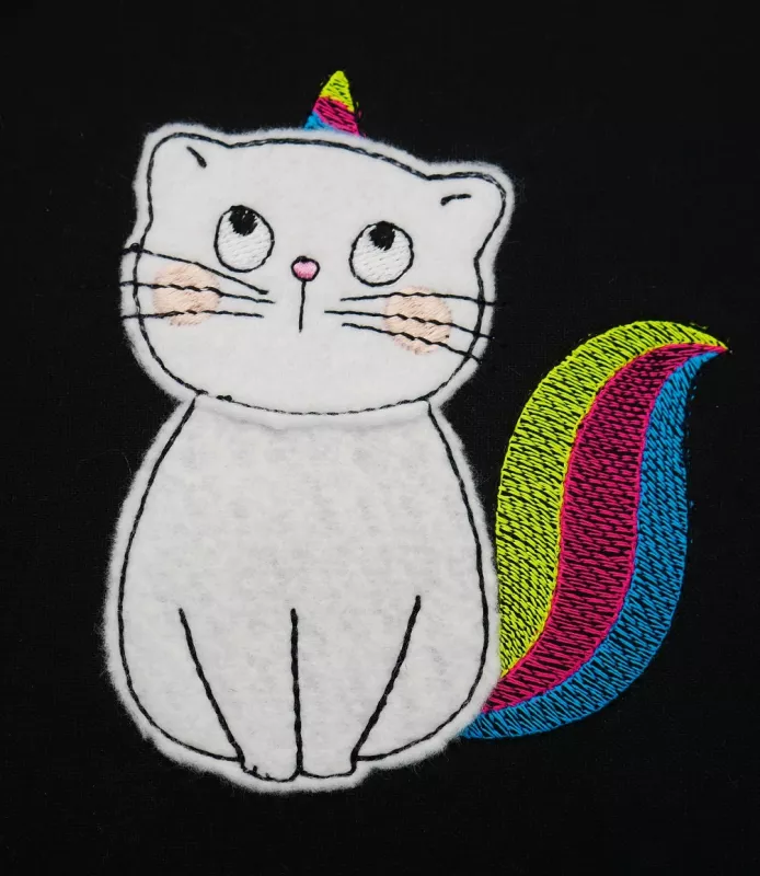 Stickdatei Set KittyCorn Doodle-Applikation inkl. ITH Anhänger, Foto mit Katze im Einhorn-Design vor schwarzem Hintergrund. Horn und Schwanz sind bunt gestickt, die Katze selbst ist aus hellem Filz.