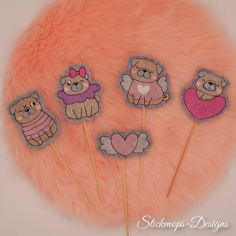 Stickdatei Set Valentinsmöpse ITH Stabdesigns für Stabdeko, Foto fünf unterschiedlicher Designs, präsentiert auf orangem Fellstück. Vier Möpse am Stab: Mops mit Zwinkerauge und Jäckchen, Mops mit Zwinkerauge, Ohrschleife und Halskrause, Mops mit Flügeln, 