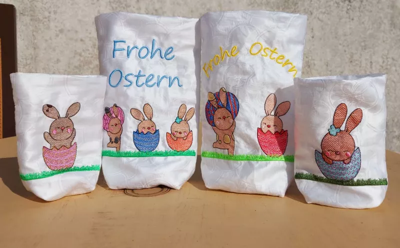 Stickdatei Set Osterhasen ITH Lichtbeutel / Utensilos, Foto zeigt 4 helle Hochkantbeutel, je bunte Bestickung: 2 kurze Beutel mit unterschiedlichem Motiv Hase in Eierschale auf Wiese; 2 lange Beutel mit 2, bzw. 3 diversen Hasenmotiven und Schriftzug "Froh