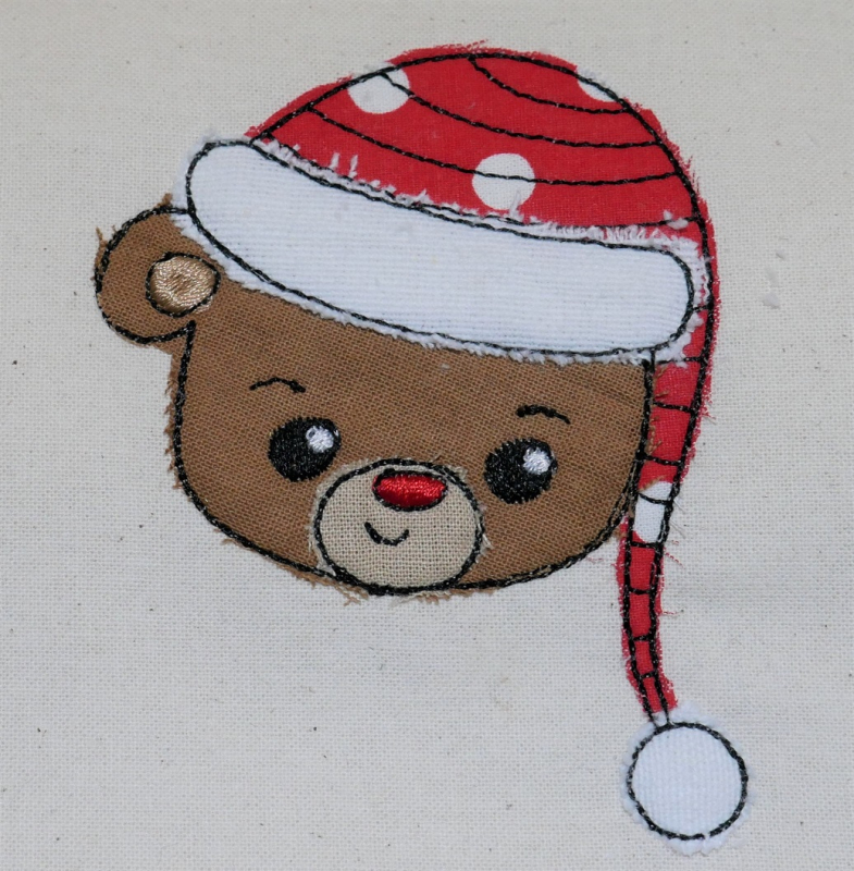 Stickdatei Set Christmas Faces Doodle-Applikationen. Foto von Applikation Teddybärenkopf mit Mütze, aufgebracht auf hellen Stoff.