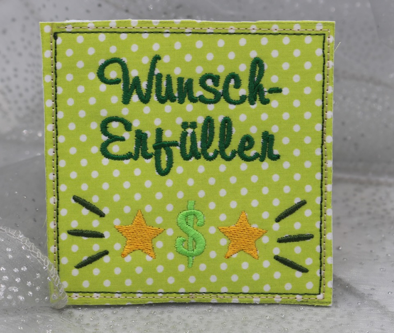 Stickdatei Set ITH Mini-Grußkarten inkl. Abwandlung zur Geschenktasche, Foto mit 1 quadratischen Ausarbeitung, präsentiert vor hellem Hintergrund. Grün-weiß gepunkteter Stoff mit Bestickung. Schriftzug "Wunscherfüller", Sterne und Dollarzeichen.