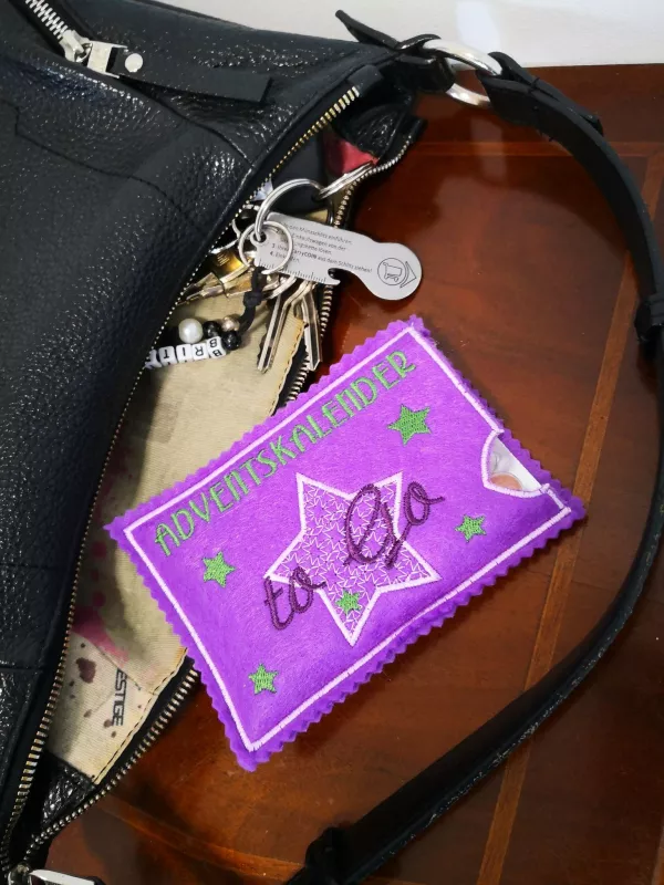 Stickdatei Set ITH Hüllen für Adventskalender to go, Foto zeigt querformatige Hülle, aus Handtasche auf 
Tisch gekippt. Grundlage pinker Filz mit Sternenstick und Schriftzug "ADVENTSKALENDER to Go.