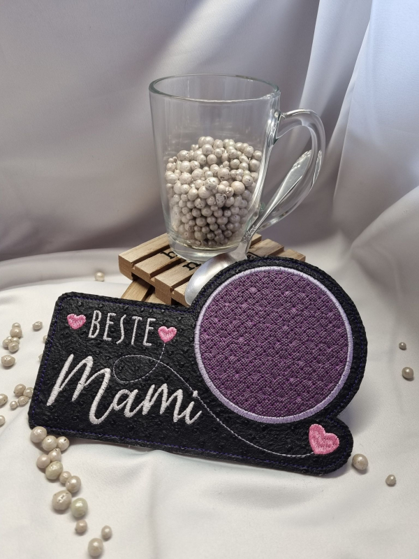 Stickdatei Set ITH Mug Rugs "die besten" inkl. Schriftzüge, Foto zeigt schmalen Tassenteppich aus dunklem Filz mit darüber hinausgehendem kreisrundem Abstellplatz mit lila Muster darin. Bestickung: "Beste Mami" mit Schnörkel und 3 rosa Herzchen.