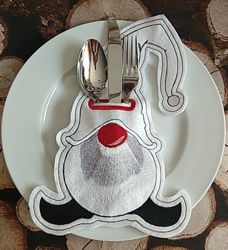 Stickdatei Set ITH Gnom Bestecktaschen und Geschenkanhänger (div. Rahmengrößen). Foto zeigt auf Teller Bestecktasche in Gnomumriss, befüllt mit Löffel/Messer/Gabel. Überwiegend hell, rote Nase, grauer Bart, schwarze Füße. Stickdatei Set ITH Gnom Bestecktaschen und Geschenkanhänger (div. Rahmengrößen). Foto zeigt auf Teller Bestecktasche in Gnomumriss, befüllt mit Löffel/Messer/Gabel. Überwiegend hell, rote Nase, grauer Bart, schwarze Füße.