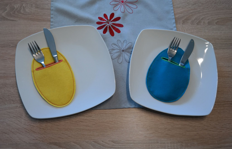 Stickdatei Set 12 ITH Bestecktaschen Blanko. Foto zeigt 2 ovale Taschen auf je einem Teller, beide befüllt mit Besteck. Einmal in gelb, einmal in dunkelbau.